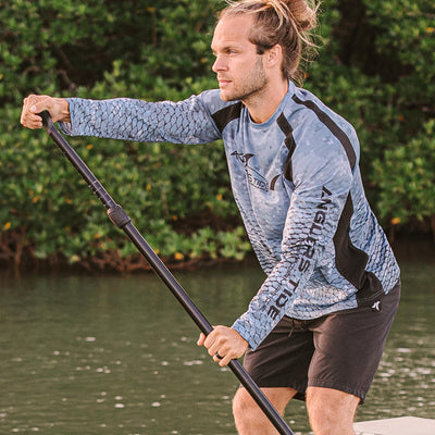 Man paddle boarding with a long sleeve fishing shirt#color_plato-carbon